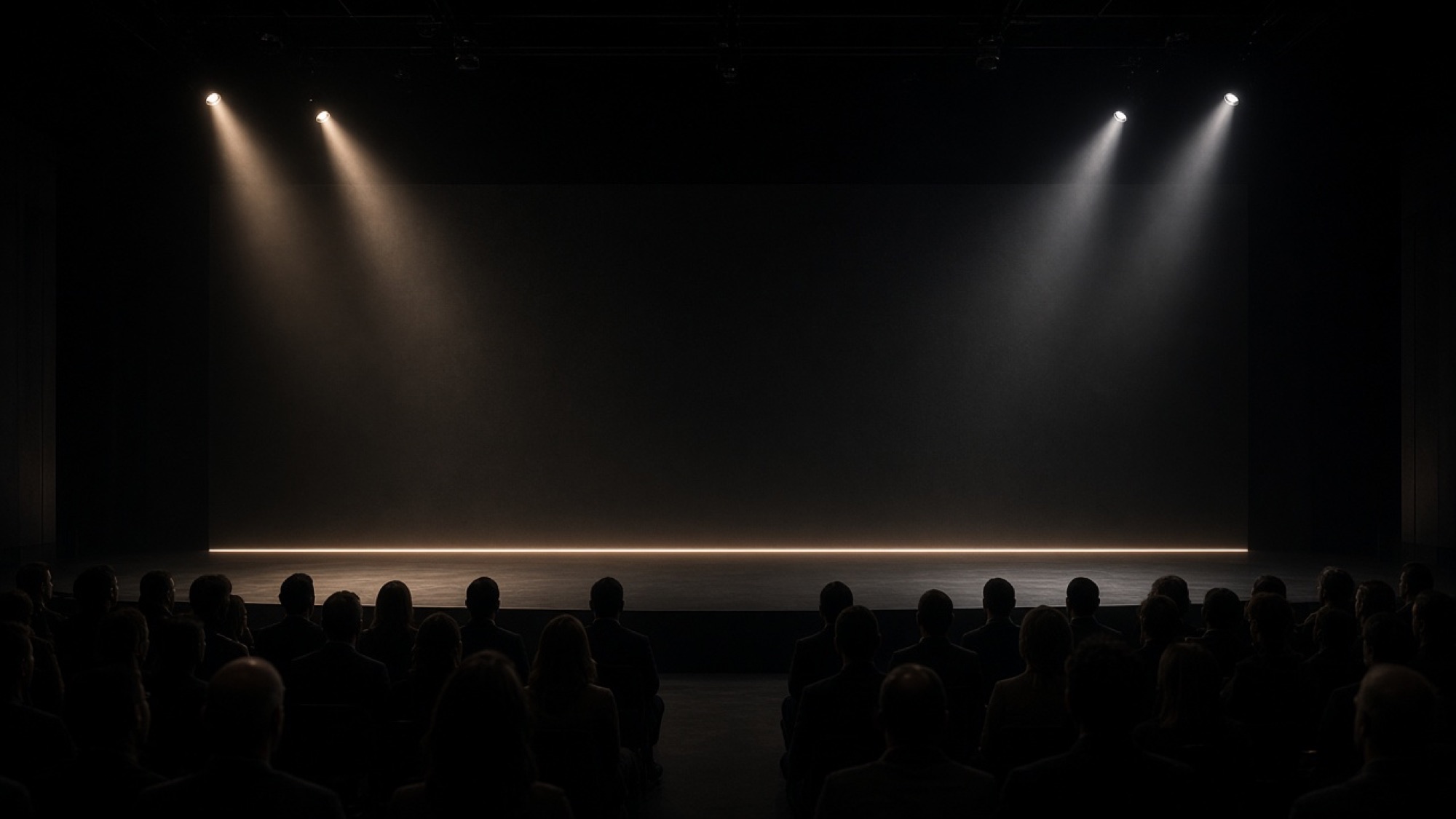 Dark stage with a line of warm light and audience silhouettes